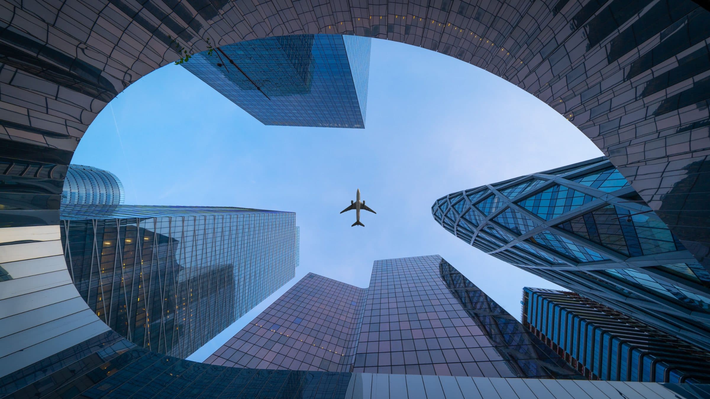 View looking up at glass skyscrapers with an airplane overhead, representing global business reach